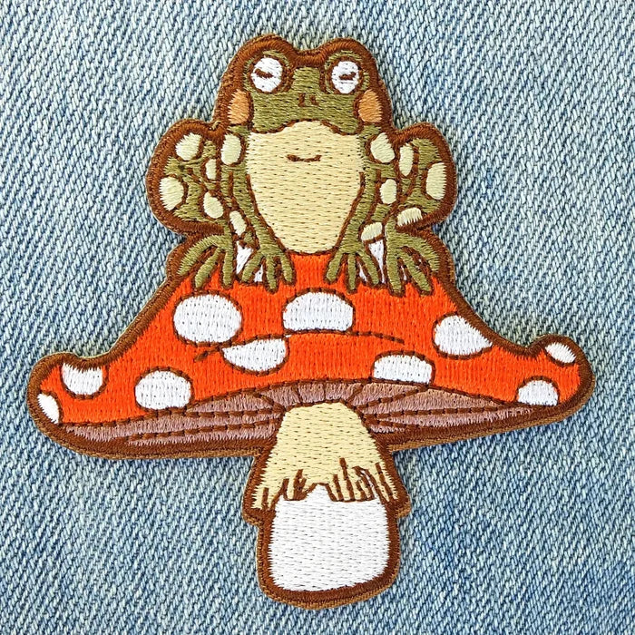 Close up of a toad and mushroom patch showing a green toad atop an orange spotted mushroom