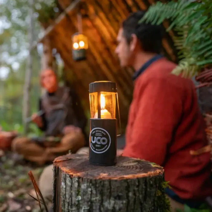 UCO original candle lantern on a tree stump with people in the background in a forest setting