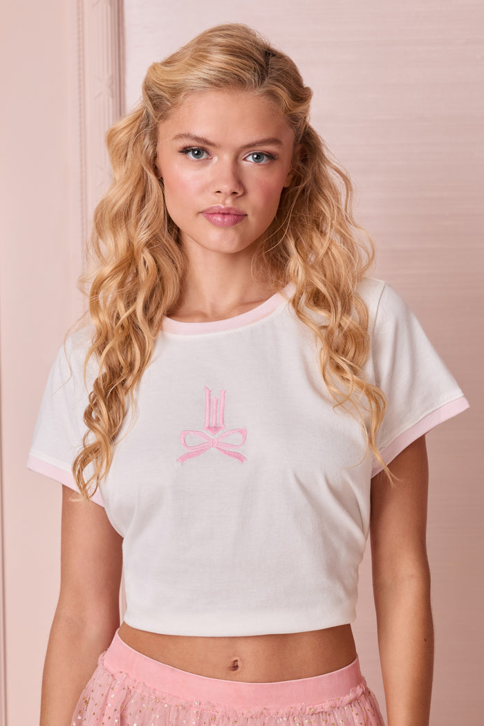 Woman wearing a white crop top with a pink logo and pink shorts against a light pink background