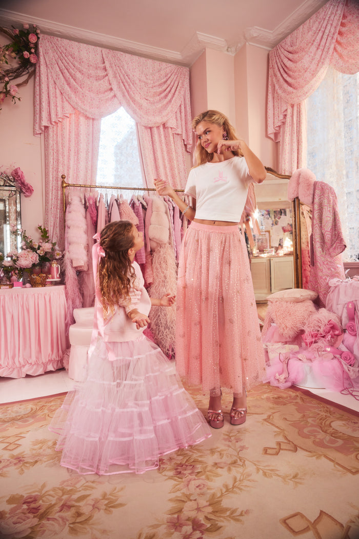 Two women in a pink-themed room with decorative curtains and furniture.