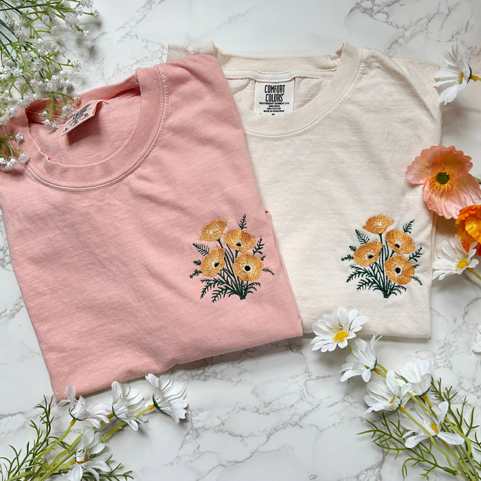 Pink Wild Poppies embroidered boxy crop tee on a marble surface with white flowers.