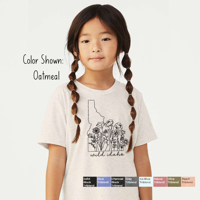 Young girl wearing an oatmeal tee featuring an Idaho outline with wildflowers and wild idaho script