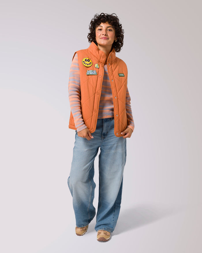 Model wearing orange patched quilted puffer vest over a striped sweater and jeans
