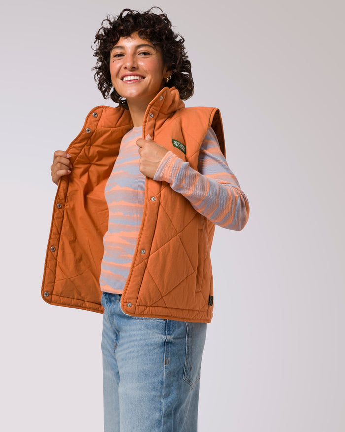 Smiling woman wearing orange quilted puffer vest over a pastel striped knit top