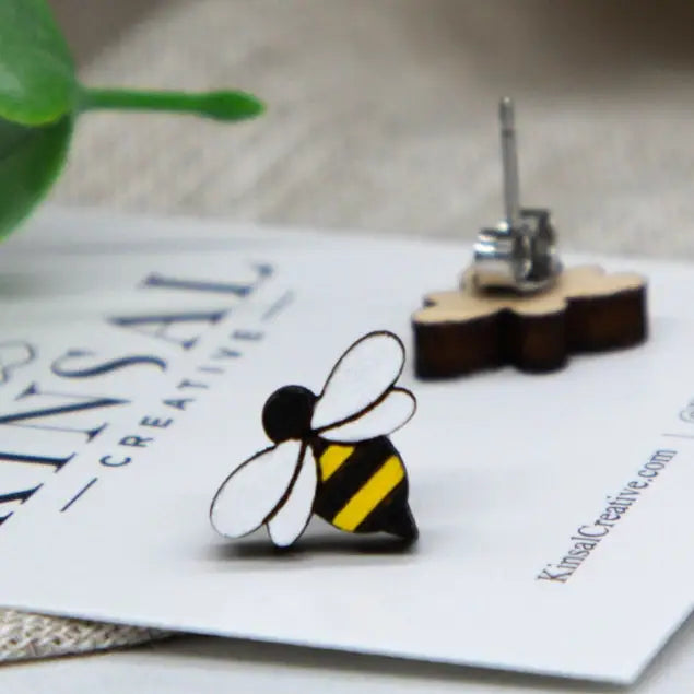 Wooden bumblebee stud earrings with white wings and yellow black striped body resting on a display card