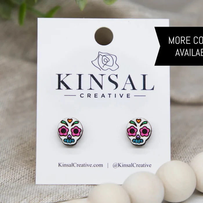 Sugar skull stud earrings with colorful designs displayed on a Kinsal Creative branded card.