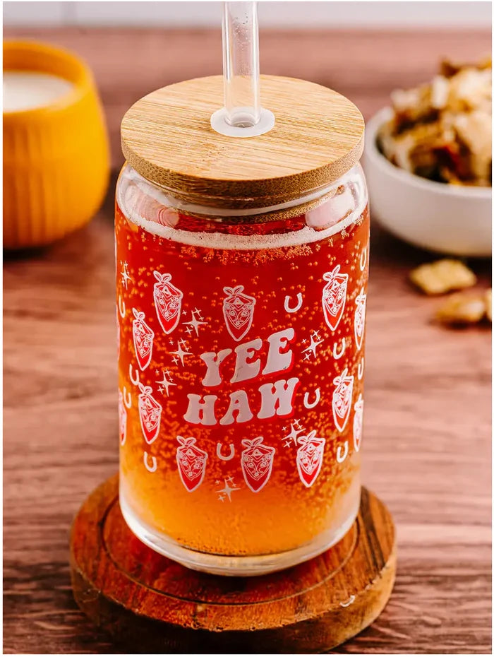 Red orange drink in a glass can with straw and bamboo lid, Yee Haw logo and mountain graphics.